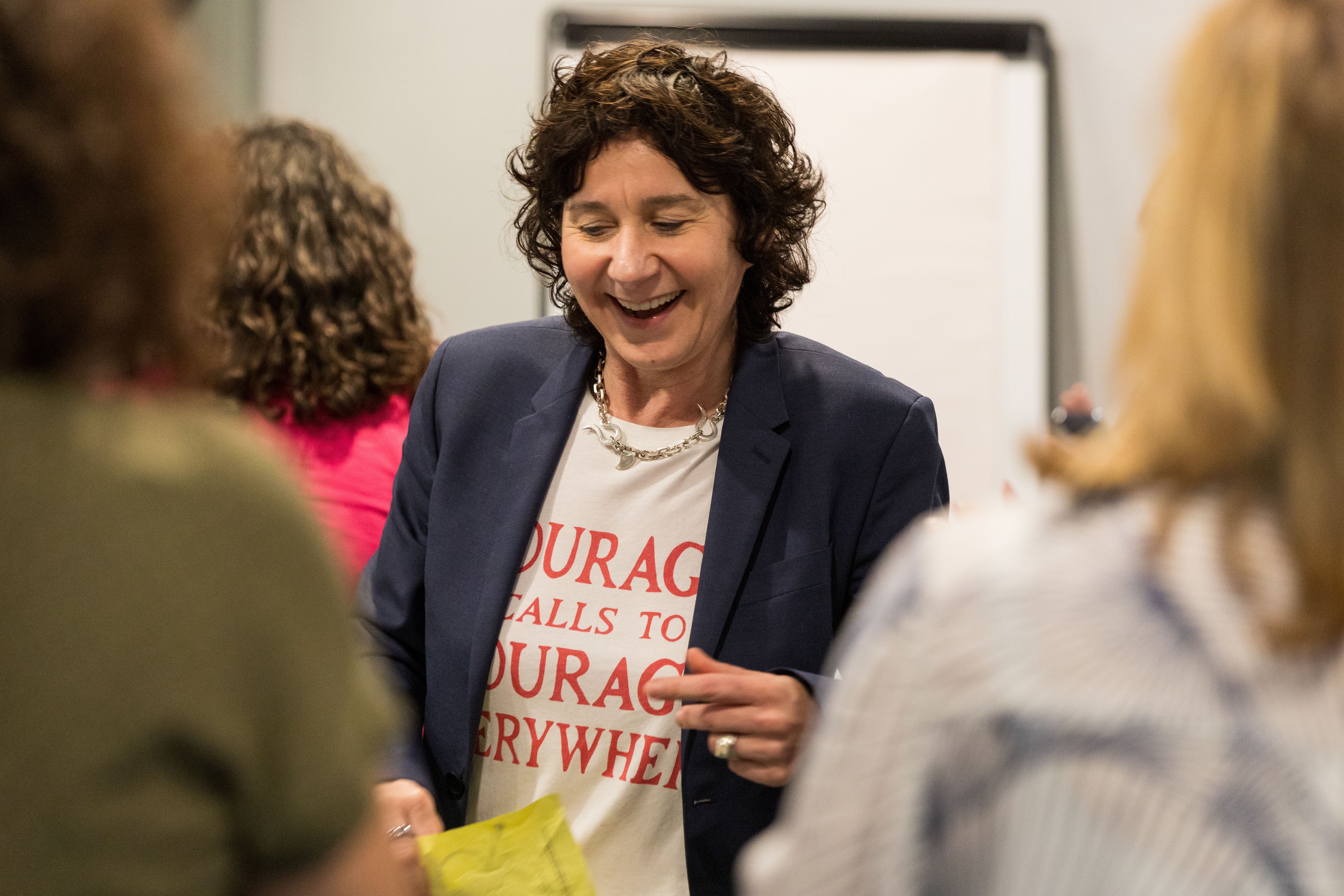 Global Warriors CEO Biba Binotti standing in a room of people (that are out of focus) looking happy/smiling