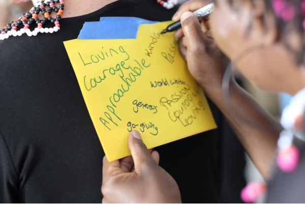 A post-it note on someone's back with a woman writing words on it. (such as loving, courage, approachable)