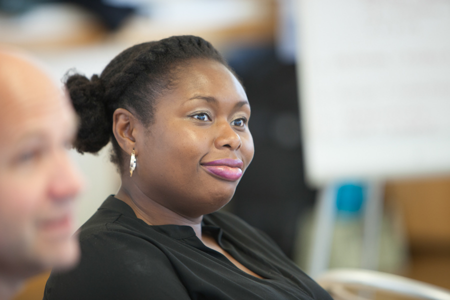 A woman and man (out of focus) at work smiling and looking in the same direction