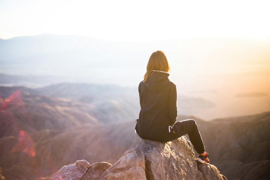 Woman sat on edge on mountain top looking at sunset